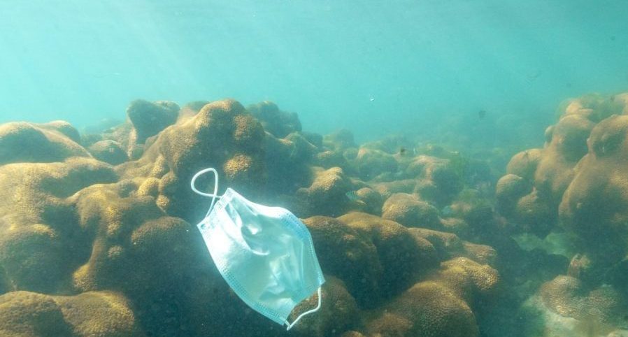 A disposable protective mask floats in the sea. Masks increase plastic pollution significantly and cause major damage to the environment.
